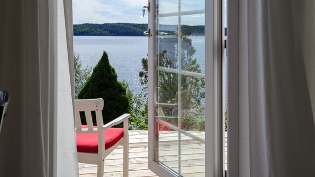 A room with a sliding glass door leading to a balcony with a wooden deck and a red chair.