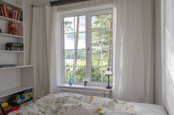A bedroom with a large window, a radiator, a lamp, and bookshelves. - House directly over the lake (Tämta)