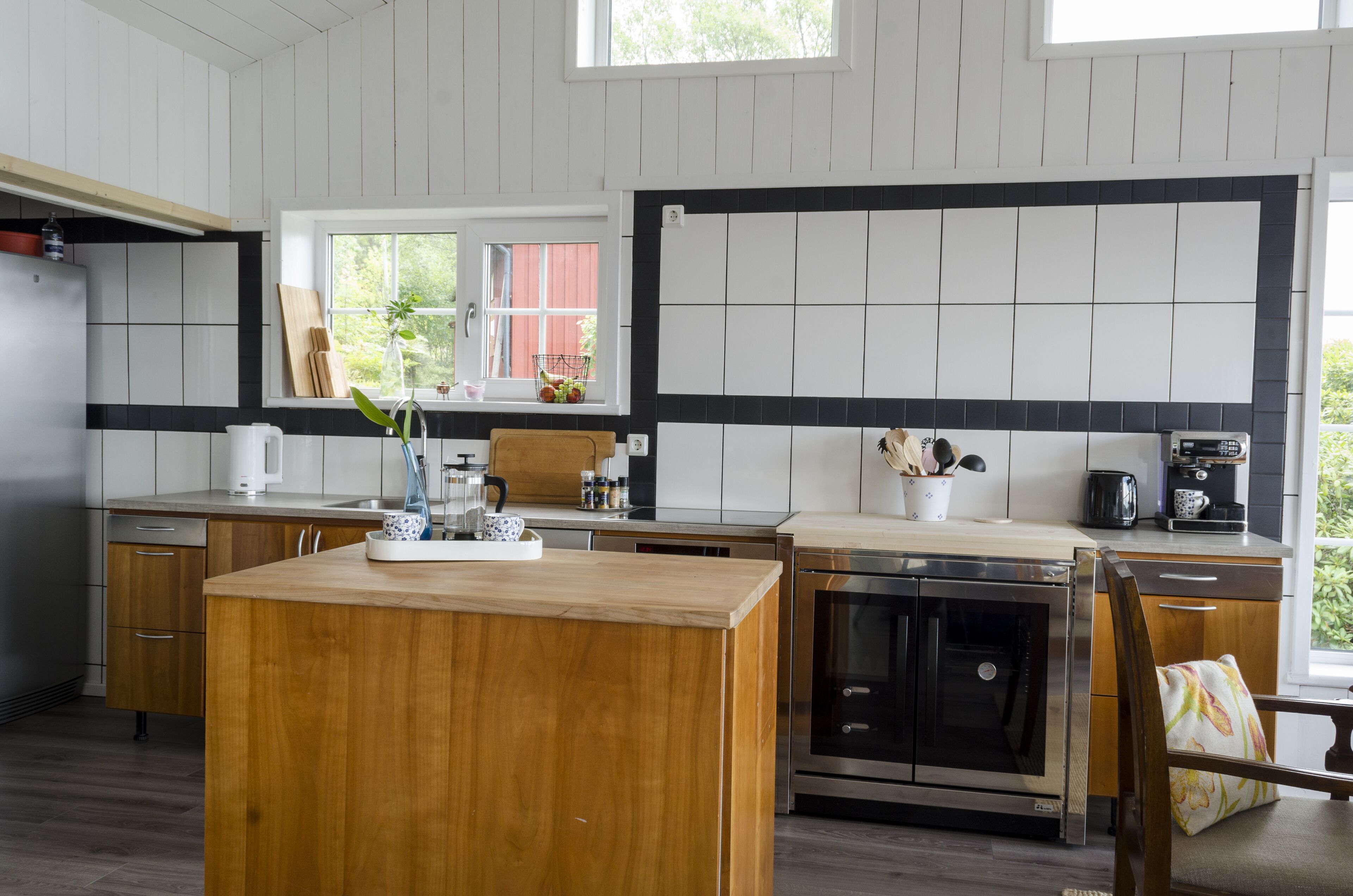 Une cuisine moderne dotée d’un îlot central en bois, d’appareils électroménagers en acier inoxydable et d’une fenêtre donnant sur un paysage verdoyant.