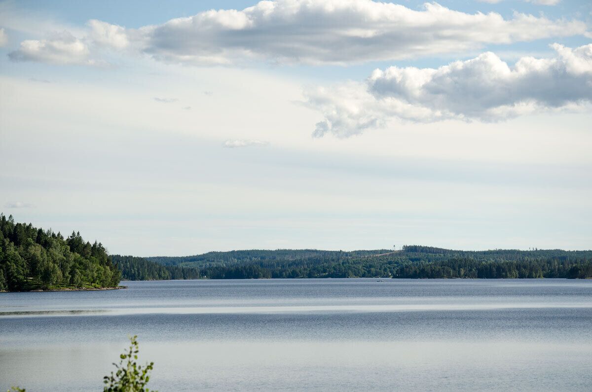 Un lac paisible, bordé d’une forêt et dominé par une colline lointaine.