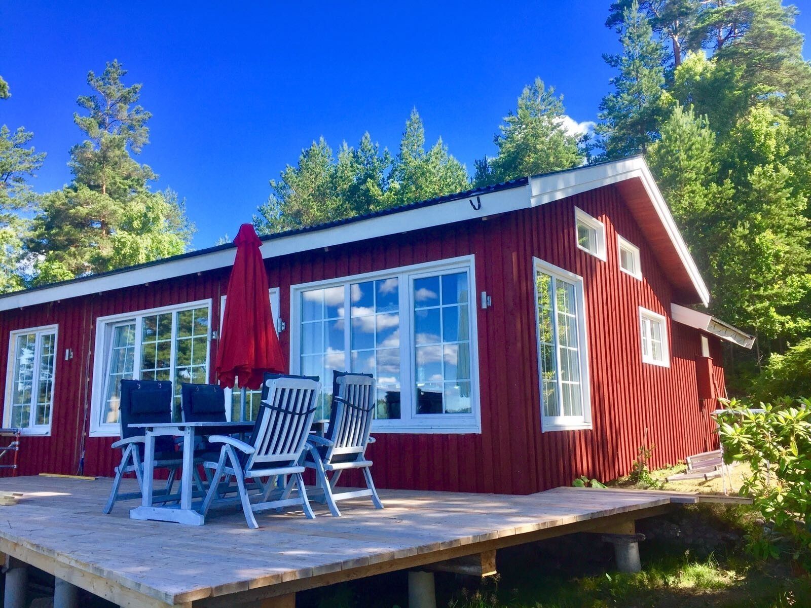 Een rode houten chalet met terras, ramen met witte kozijnen en buiten zitplaatsen.