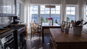 A kitchen with a view of the sea, wooden cabinets, a coffee machine, and a dining area with chairs and a table.