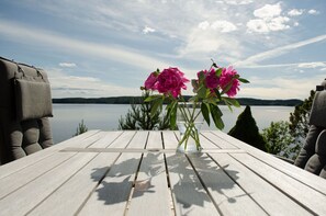 Et træbord med en vase med lyserøde blomster og udsigt til et sø.