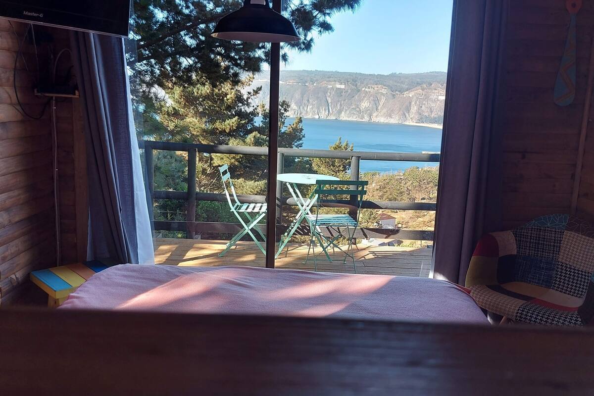 Una habitación con una cama, vista a un lago y un balcón con sillas y una mesa.
