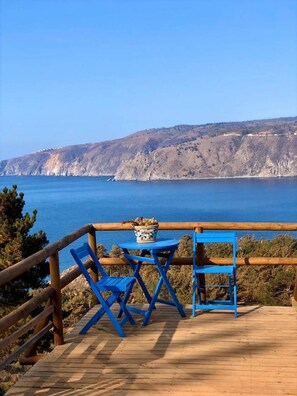 Une terrasse en bois avec une table et des chaises, donnant sur une étendue d’eau et un paysage montagneux.