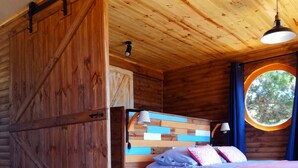 Una habitación acogedora de estilo cabaña, con una cama, una mesita pequeña y un ventanal redondo.