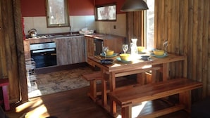 Una cocina rústica con armarios de madera, una mesa de comedor con cuencos amarillos y copas de vino, y una lámpara colgante.