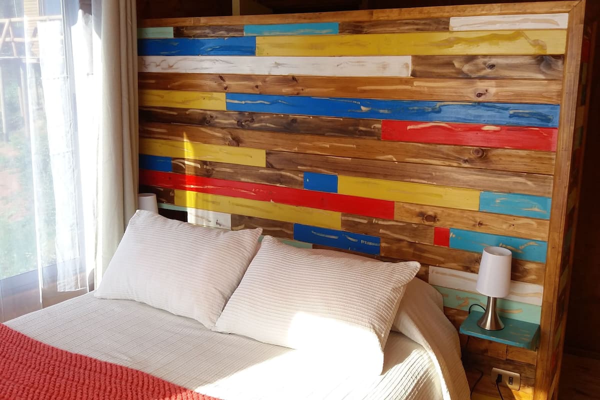 Una cama con ropa de cama blanca en una habitación con un cabecero de madera colorida.