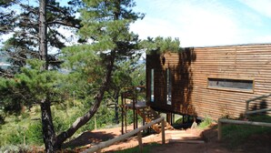 Una cabaña de madera con un porche y escaleras, rodeada de árboles y un sendero de tierra.