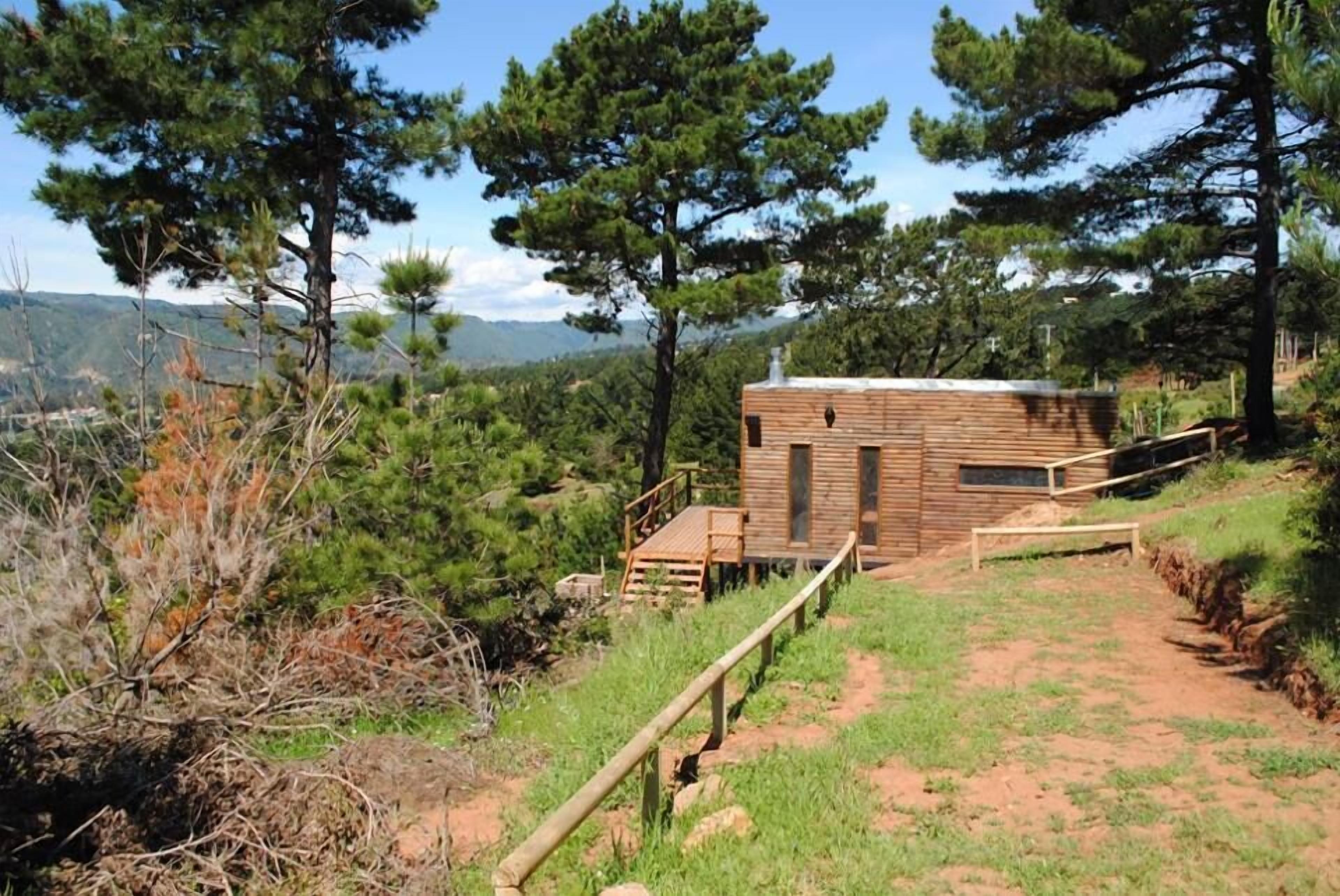 Una cabaña con fachada de madera, un pequeño balcón y un camino de tierra que la lleva.