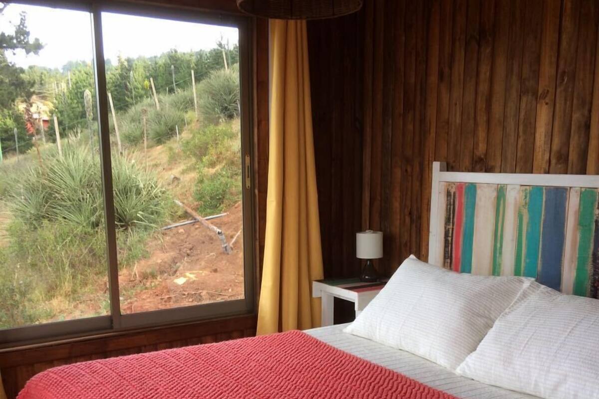 Un dormitorio con una cama grande, paredes de madera, una ventana con cortinas y vistas al exterior.