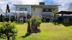 A modern two-story house with a covered patio, a small garden, and a staircase leading to the entrance.