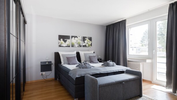 A modern bedroom with a bed, bedside tables, a bench, and a large window.