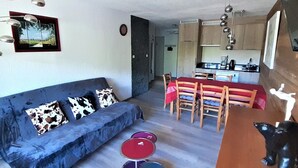 Um espaço de estar compacto com sofá, mesa de jantar com cadeiras, área de cozinha e uma pequena estátua.