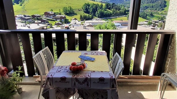 Varanda com mesa posta para dois, com vista para uma paisagem montanhosa.