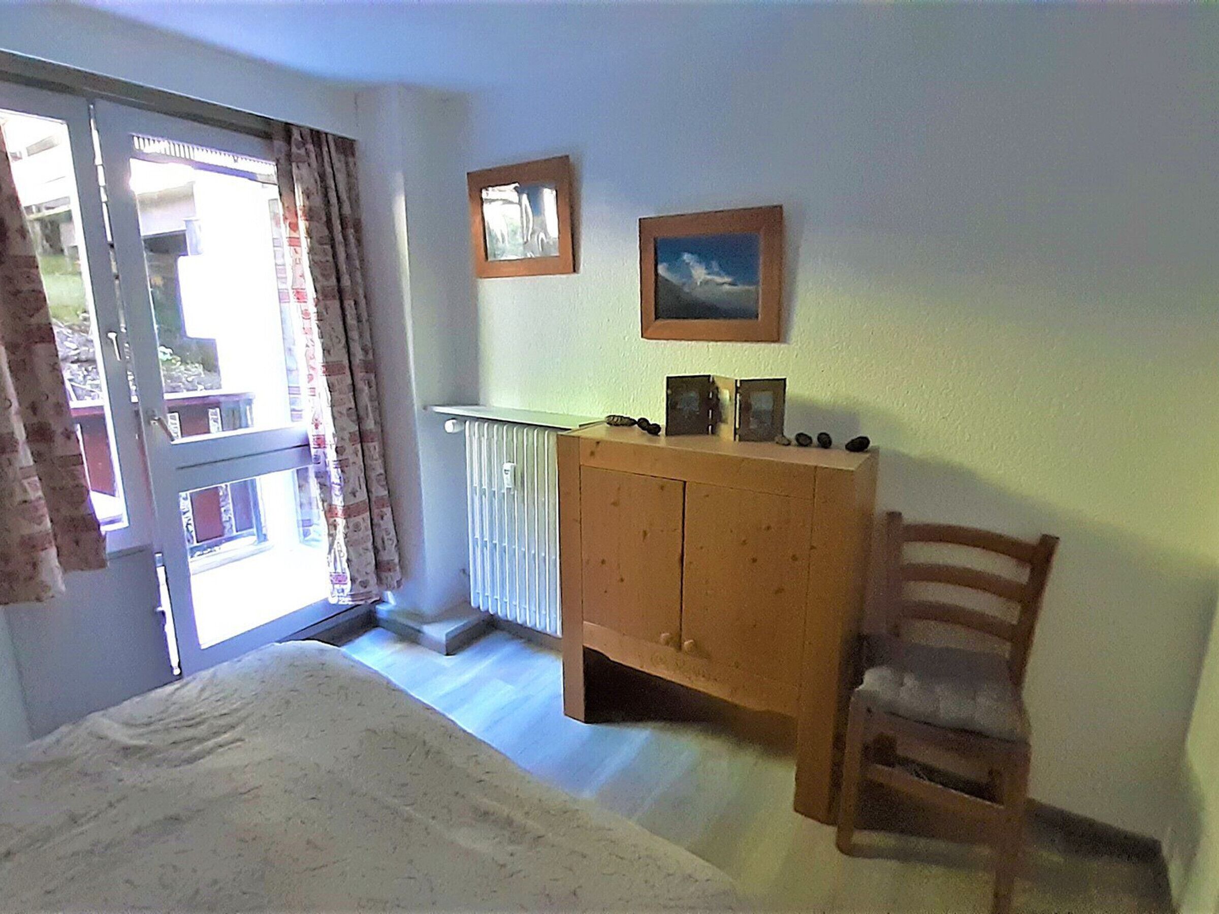 A room with a wooden cabinet, a chair, a radiator, and two framed pictures on the wall.