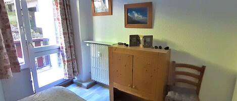 A room with a wooden cabinet, a chair, a radiator, and two framed pictures on the wall.