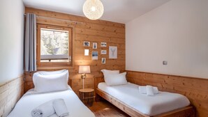 Una habitación con dos camas de madera, una ventana con cortinas, una lámpara de pared y cuadros enmarcados.