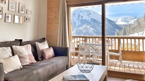 Una sala de estar acogedora con un sofá, almohadas y una mesita de centro. Un ventanal ofrece vistas a montañas cubiertas de nieve.