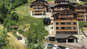 Un refugio de montaña con varios balcones de madera y un telesilla al fondo.