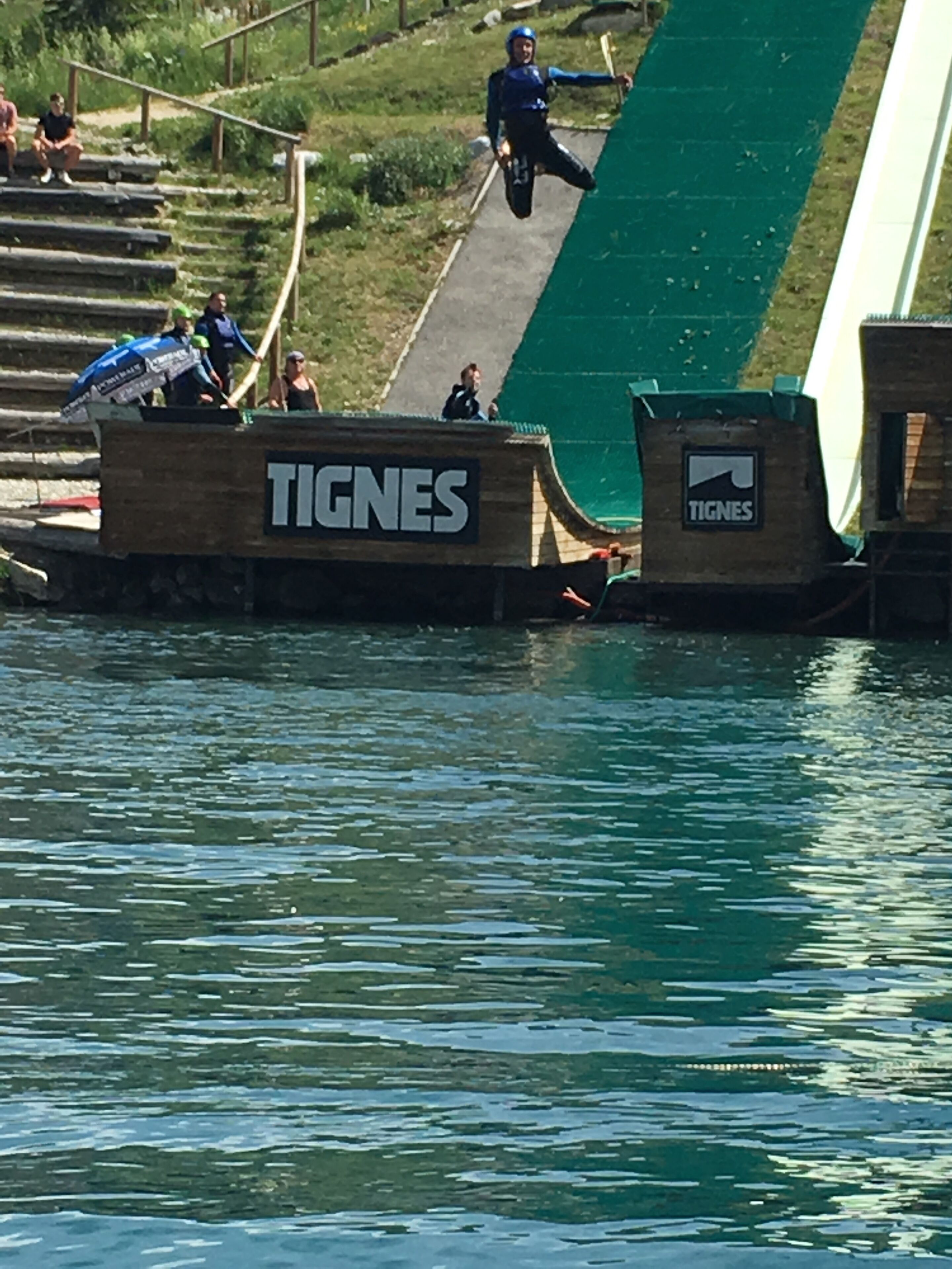A water slide with a TIGNES logo, surrounded by a grassy area and a few people.