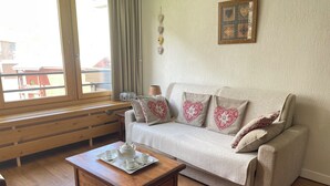 Uma sala de estar acolhedora com um sofá, uma mesa de centro de madeira e uma janela com vista para móveis de exterior.