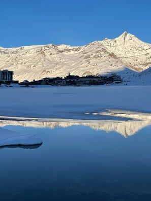 Une montagne enneigée se reflétant dans un plan d’eau calme, avec des bâtiments au premier plan.