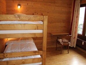 Une chambre avec un lit superposé en bois, une petite chaise et une étagère.