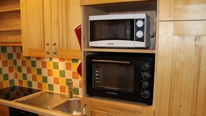 Cocina con gabinetes de madera, un lavamanos de acero inoxidable, un lavavajillas Bosch, un microondas blanco y un horno negro.