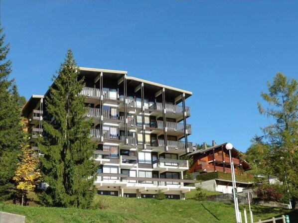 A multi-story building with balconies, surrounded by trees and greenery.