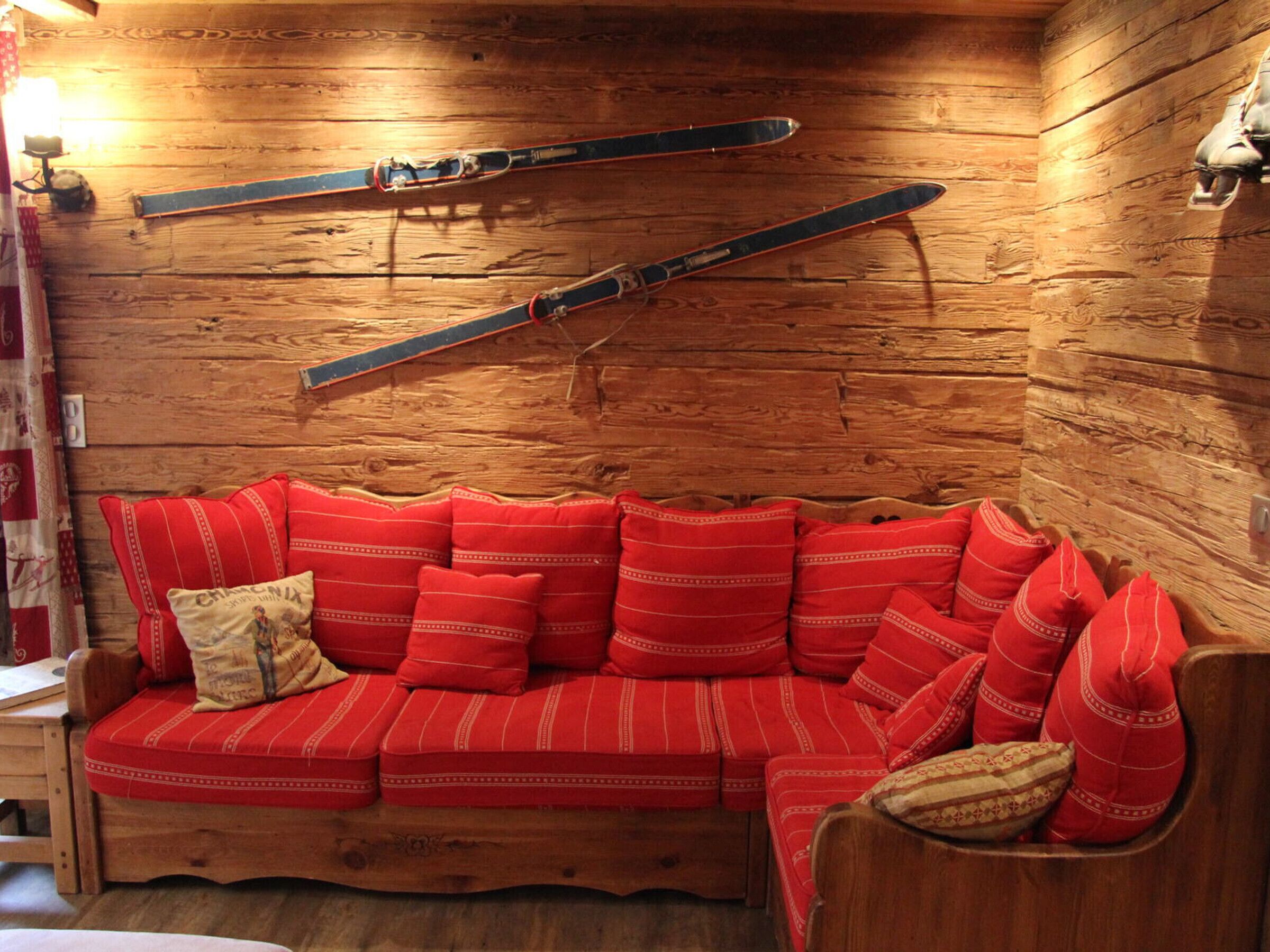 Een gezellig interieur van een chalet met een houten wand, een rode gestreepte bank en ski's erboven.