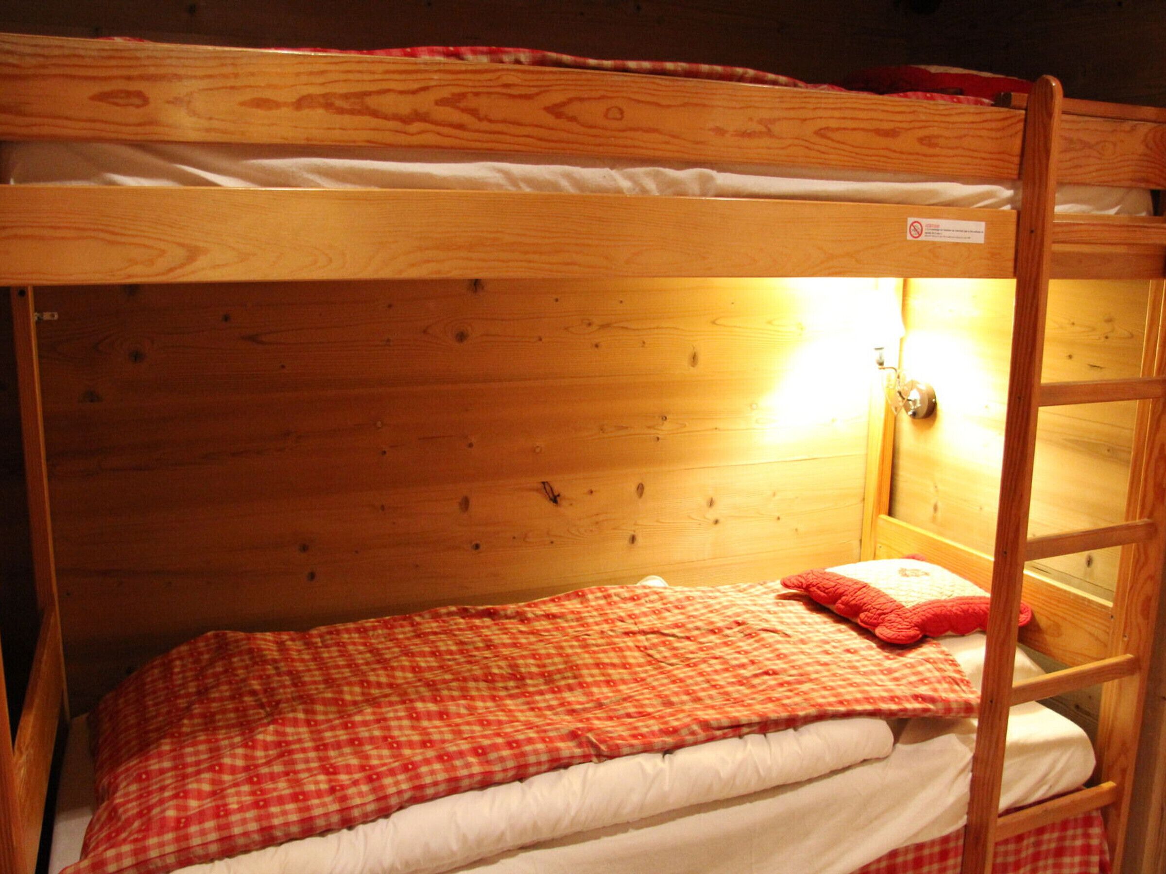 A bunk bed with a red and white checkered blanket, a wooden headboard, and a small window with a light source.