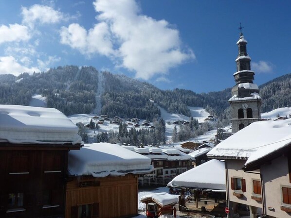 A snowy village with wooden buildings, a church with a clock tower, and a mountain backdrop.