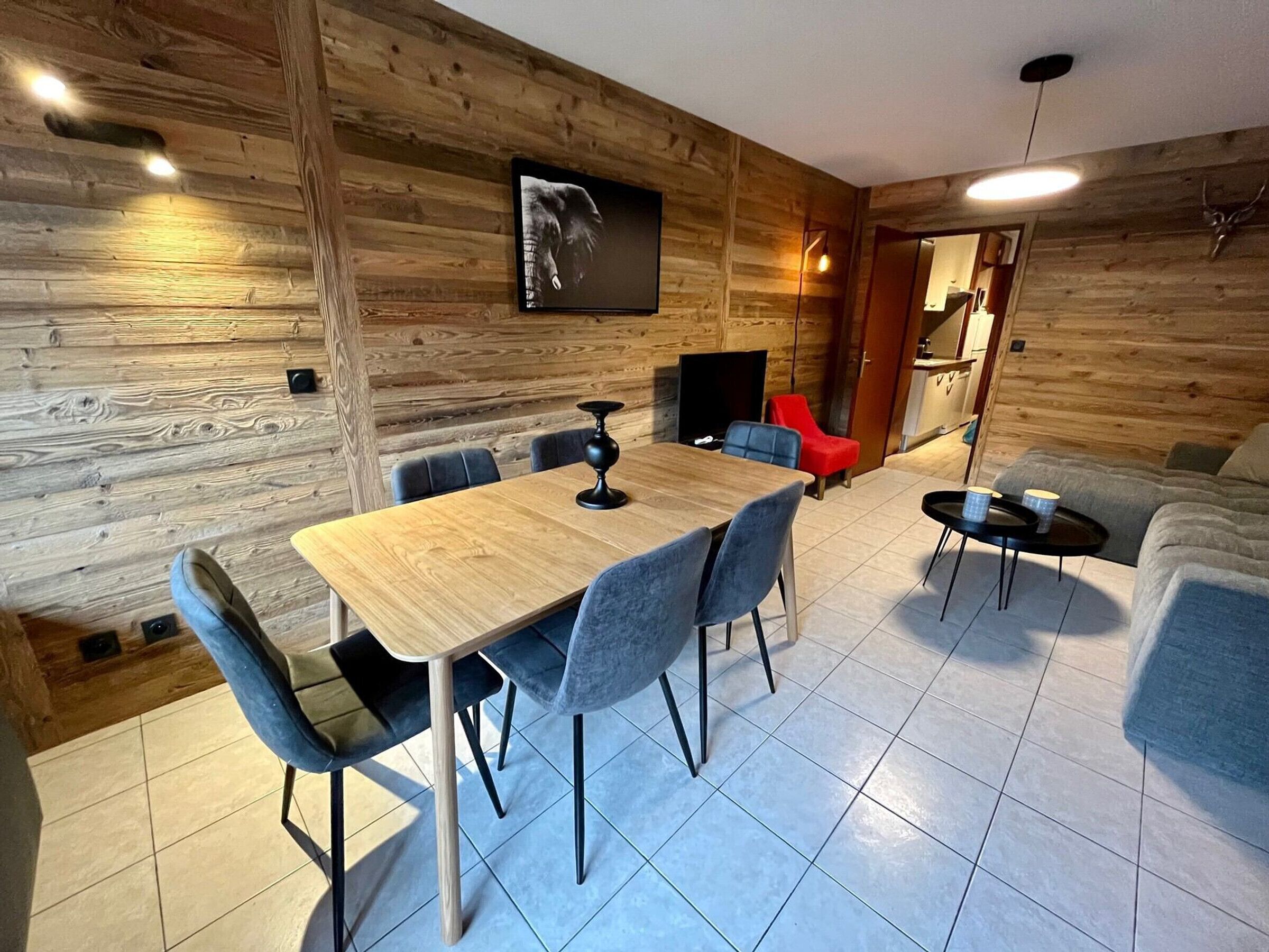 Een modern interieur met een houten wand, een eettafel met stoelen, een bank, een televisie en een bijzettafeltje met kopjes.