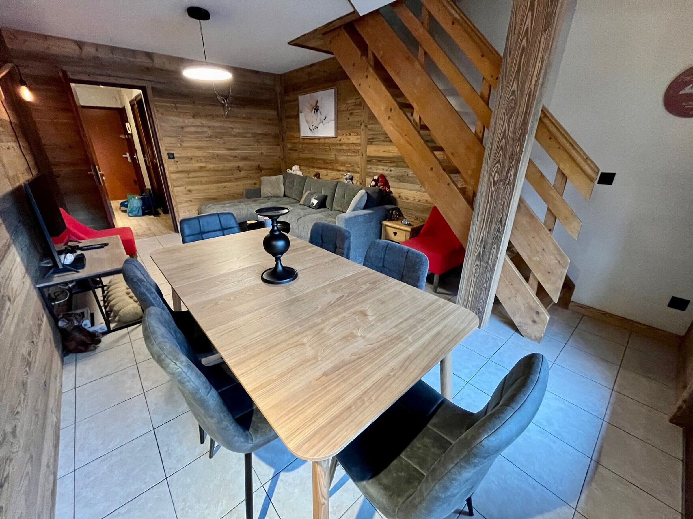 A modern dining area with a wooden table and chairs, a staircase, and a cozy living space with sofas and a TV.