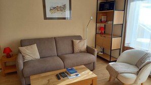 A living room with a sofa, a chair, a coffee table, a bookshelf, and a lamp. - Cosy Studio with Balcony in La Clusaz Center, Near Slopes, Sleeps 4 (La Clusaz)