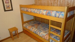 A bunk bed with patterned bedding, a small wooden stool, and a wooden wall with framed pictures. - Cosy Studio with Balcony in La Clusaz Center, Near Slopes, Sleeps 4 (La Clusaz)