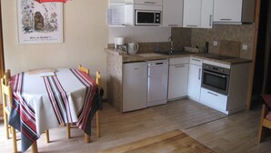 A compact kitchen with white cabinets, a microwave, a coffee maker, and a dishwasher. There's a dining table with a striped tablecloth and chairs. - Cosy Studio with Balcony in La Clusaz Center, Near Slopes, Sleeps 4 (La Clusaz)