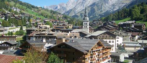 A traditional European village with historic buildings, a prominent church tower, and mountainous backdrop.