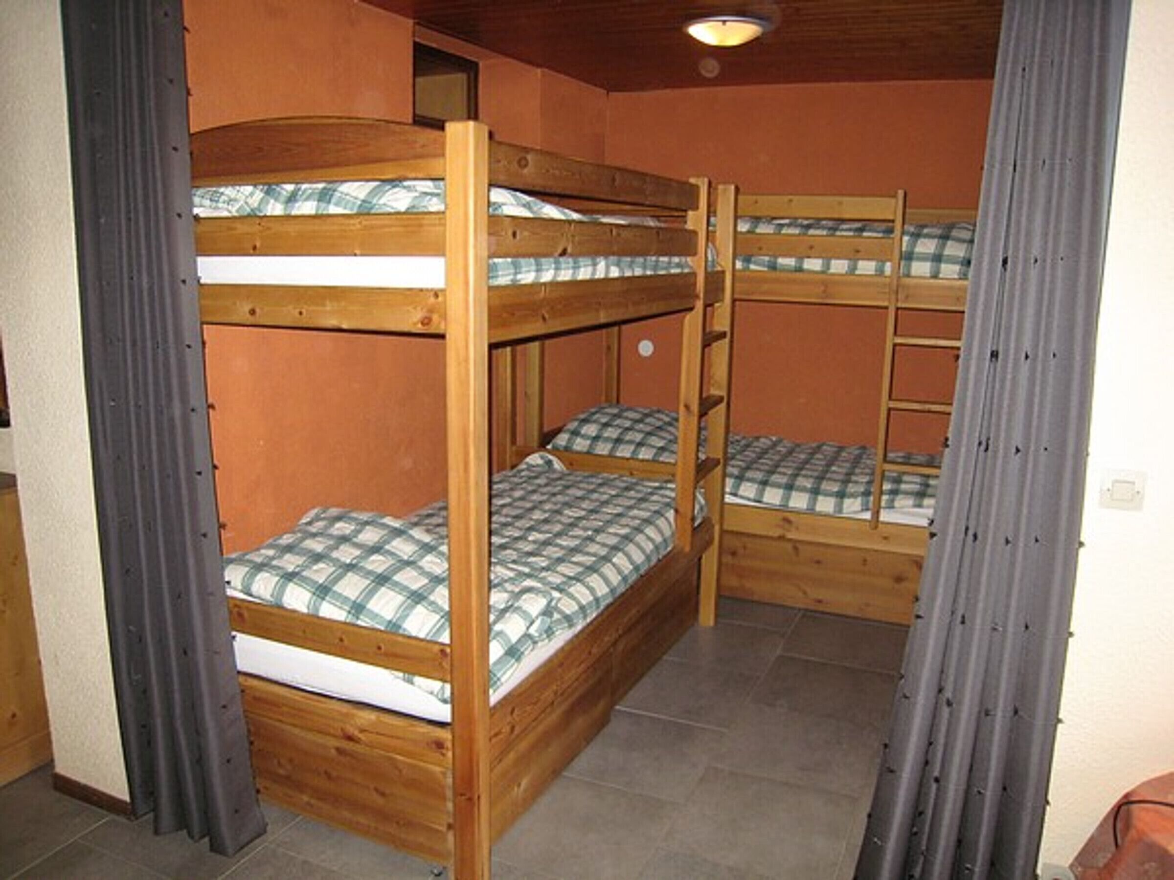 A bunk bed room with wooden frames and plaid bedding.