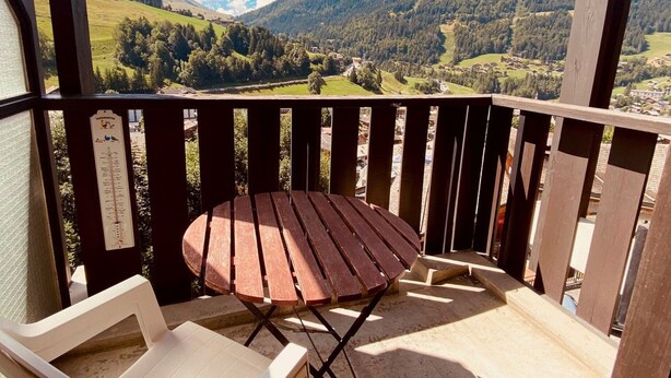 Une terrasse en bois avec une table et des chaises, offrant une vue sur un paysage montagneux.