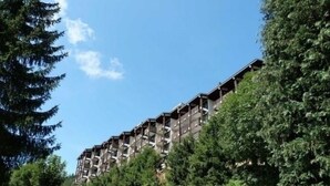 Un immeuble à plusieurs étages doté de balcons, entouré d’une végétation luxuriante et d’arbres.