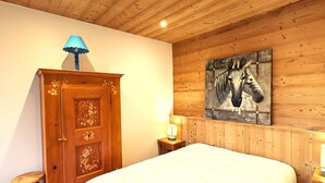 A wooden-paneled room with a bed, a wooden cabinet with floral carvings, a zebra painting on the wall, and two bedside lamps. - Cozy apt 4-6 pers balcony, ski-in/ski-out, covered parking (La Clusaz)