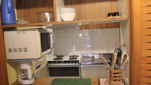 Een kleine keuken met een magnetron, fornuis en spoelbak.