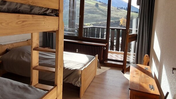 Een houten stapelbedkamer met uitzicht op een bergachtig landschap door grote ramen.