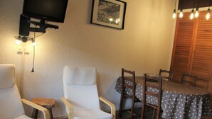 Een knus ingerichte kamer met een aan de muur bevestigde televisie, een lijst met een afbeelding en een tafel met stoelen.