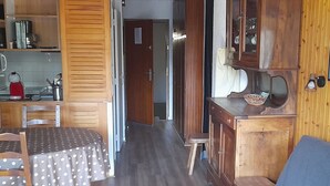 Een gezellige woonkamer met een blauwe bank, een houten eettafel met een tafelkleed met stippen, en een keuken met houten kastjes en een koffiezetapparaat.