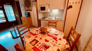 A cozy kitchen with white cabinets, a microwave, and a sink. There's a round table with a festive tablecloth and chairs. - Cozy Studio with Balcony, Near Ski Lift & Parking, La Clusaz (La Clusaz)
