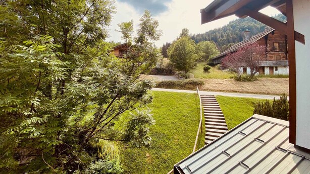 A residential area with a wooden staircase leading to a metal roofed structure, surrounded by lush greenery and traditional buildings. - Cozy Studio with Balcony, Near Ski Lift & Parking, La Clusaz (La Clusaz)