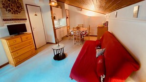 A cozy living room with a red sofa, wooden cabinets, a television, and a dining area with a table and chairs. - Cozy Studio with Balcony, Near Ski Lift & Parking, La Clusaz (La Clusaz)